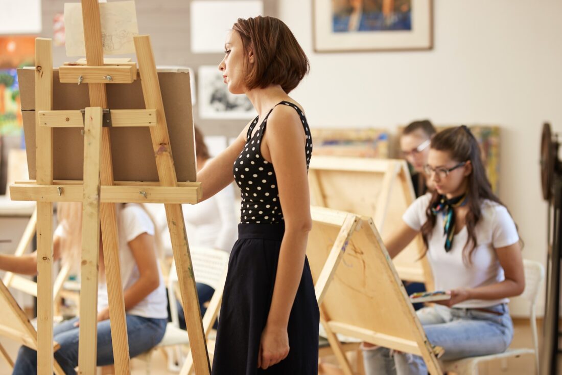 Charming drawing teacher in the beautiful dress shows drawing technique at the easel in the art